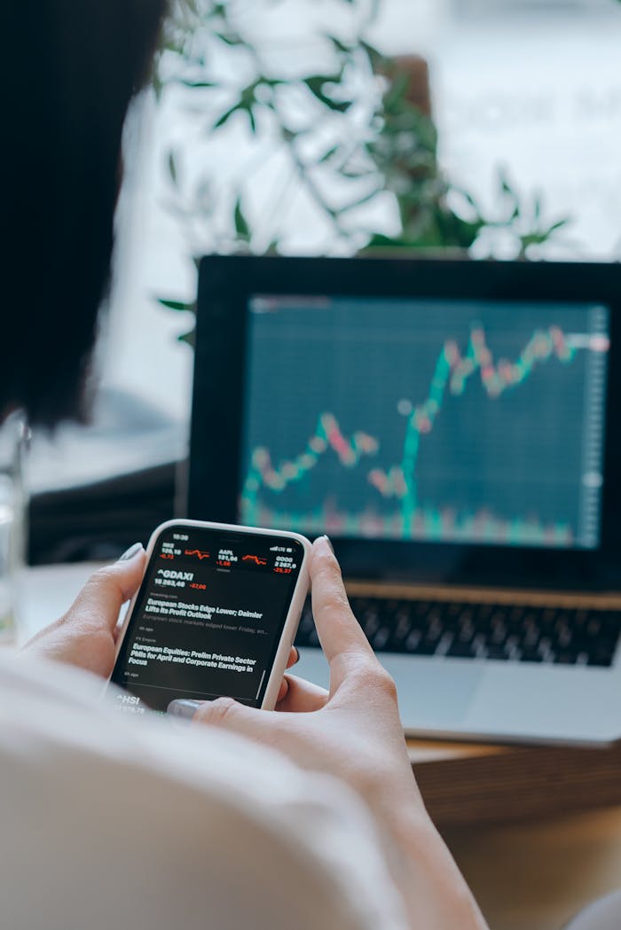 Person using smartphone for stock market analysis at home office.